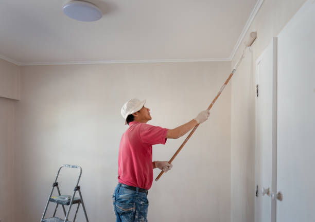 Painter on a ladder applying paint to an interior wall